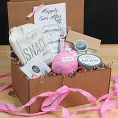 an open box with some items in it on a wooden table next to pink ribbon