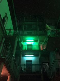 an apartment building lit up with green light at the top and second story balcony area