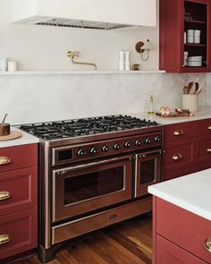 a stove top oven sitting inside of a kitchen next to red cabinets and counter tops