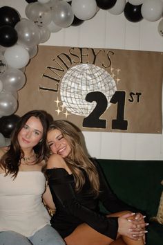 two women sitting next to each other in front of balloons and a sign with the number 21 on it