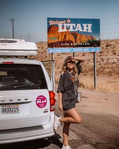 a woman standing next to a white van in front of a welcome to utah sign