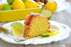 a slice of cake on a plate with lemons and limes in the background