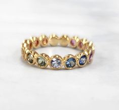 a gold ring with multicolored stones on the inside and outside, sitting on a white surface