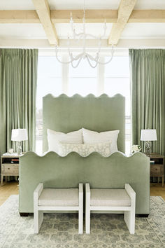 a green bed with white pillows and two benches in front of the headboard,