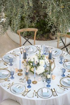 the table is set with blue and white plates, silverware, flowers and candles