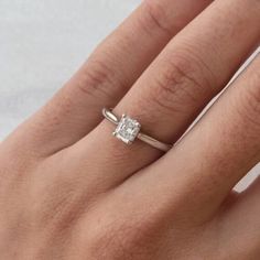 a woman's hand with a white diamond ring on her left hand and the other hand holding an engagement ring