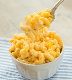 a spoon full of macaroni and cheese is being lifted from a white bowl