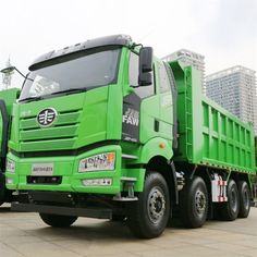 a green dump truck parked in front of a tall building with skyscrapers behind it