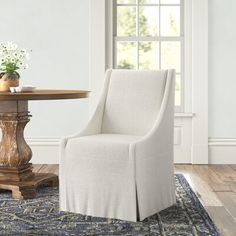 a white chair sitting in front of a table on top of a blue rug next to a window