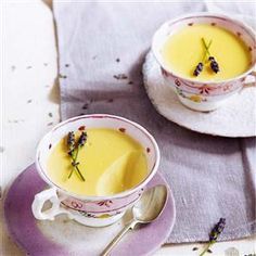 two cups filled with soup sitting on top of a purple and white saucer next to a spoon