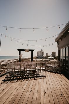 an empty deck with chairs and string lights on the beach in front of some buildings