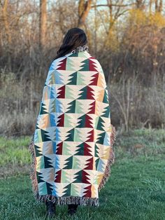 a woman standing in the grass wearing a blanket