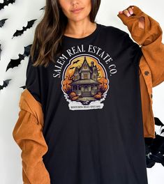 "👕MORE T-SHIRTS: tinyurl.com/SwagTshirts 👕MORE SWEATSHIRTS: tinyurl.com/SwagSweatshirts Welcome to the spooky world of real estate with our \"Salem Real Estate Co. Halloween Shirt\" - the perfect attire for all the realtors and real estate agents who dare to venture into the mysterious realm of property deals during the Halloween season! Product Details: - Design: Our exclusive shirt showcases a captivating blend of Halloween charm and professional pride. The front features a tastefully designed logo with \"Salem Real Estate Co.\" emblazoned in a hauntingly elegant font, surrounded by subtle ghostly silhouettes, witch hats, and bats. It's a delightful nod to the enchanting spirit of the season. - Material: Crafted from high-quality, breathable fabric, this shirt guarantees all-day comfor Fall Band Merch Crew Neck Shirt, Fall Band Merch Shirt With Crew Neck, Fall Crew Neck Shirt Band Merch, Fall Crew Neck Shirt With Band Merch Style, Pre-shrunk Black Shirt For Fall, Spooky Long Sleeve T-shirt With Custom Print, Spooky Long Sleeve T-shirt With Screen Print, Spooky Long Sleeve Screen Print T-shirt, Spooky Long Sleeve Shirt With Letter Print