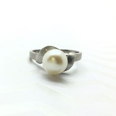 This vintage ring features a 8mm round cultured pearl, creamy white with a beautiful high lustre all set in 10 karat white gold. Curled around the pearl are two 10 karat white gold leaves in a brushed texture. Please message me if you have any questions. Thank you for looking! Metal: 10 karat white gold  Gemstone: Cultured Pearl  Period: 1960's Total weight: 2.77 grams  Markings: 14k (tested lower) Size: 7  Unless stated otherwise, all the items we sell are pre-owned/pre-loved. It is normal for White Solitaire Pearl Ring, Round Cut, White Solitaire Pearl Ring, Classic White Gold Akoya Pearl Ring, Classic White Akoya Pearl Ring, Timeless Pearl White Pearl Ring For Anniversary, Classic White Pearl Ring, Timeless White Round Cut Pearl Ring, White Timeless Round Cut Pearl Ring, Timeless White Akoya Pearl Ring