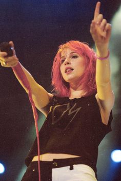 a woman with pink hair is holding her hand up in the air while performing on stage