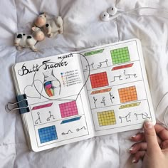 a person is holding an open book on a bed with stuffed animals next to it