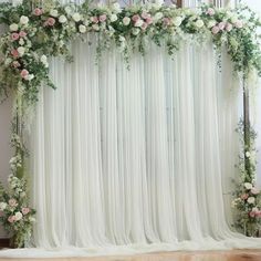 a white curtain with flowers and greenery on the top is draped in front of a mirror