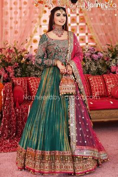 a woman in a green and pink lehenga standing under a chandelier