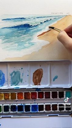 someone is painting on the beach with watercolors