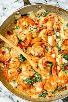 a skillet filled with shrimp and vegetables on top of a marble countertop next to a wooden spoon