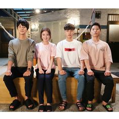 four people are sitting on a bench in front of a building and posing for the camera