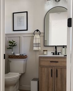 a white toilet sitting next to a wooden cabinet in a bathroom under a large mirror