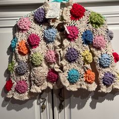 a crocheted jacket hanging from a hook on a white door with colorful flowers