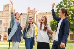 four young people standing in front of a building with their hands up