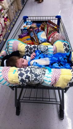 a baby is sleeping in a shopping cart filled with snacks and other items, on the floor