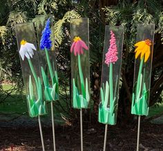 three wooden sticks with flowers painted on them in front of some grass and trees,