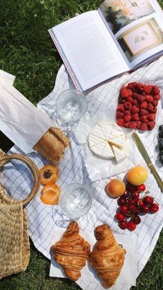 an open book on top of a table filled with fruit and pastries next to bread