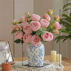 pink roses in a blue and white vase on a table next to some candles,