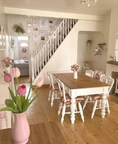 a dining room table and chairs with pink flowers in a vase on the floor next to it