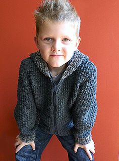 a young boy standing in front of a red wall with his hands on his hips