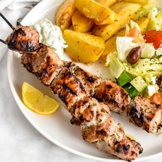 a white plate topped with meat and veggies next to lemon wedges on top of a table