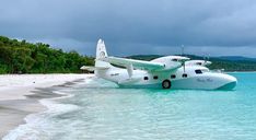 an airplane sitting on top of the ocean next to a sandy beach with blue water