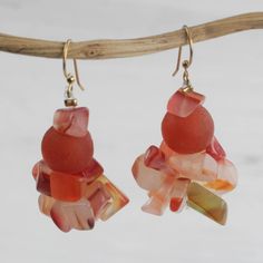 the earrings are made out of glass and have pink flowers on them, hanging from a branch