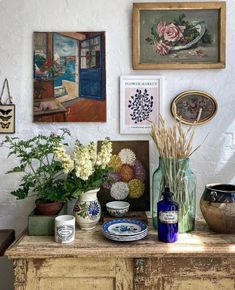 there are many vases and flowers on the table in front of the wall with pictures above them