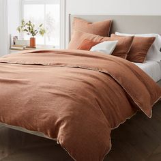 a bed with an orange comforter and two pillows on it, in front of a window