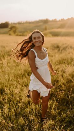 a woman in a white dress is running through the grass with her hair blowing in the wind