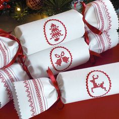 four white towels with red embroidered designs on them sitting in front of a christmas tree