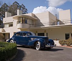 an old blue car parked in front of a large white building with balconies