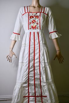 "This dress is so special. It is a vintage 60s/70s Mexican pin tucked white dress. The dress has a square neckline, that is trimmed with red ribbon and small lace ruffles, is fitted to the waist with a floral embroidered bodice that is also finished on the side with red ribbon, it has 3/4 sleeves with a flared lace cuff and red ribbon trim, The skirt is a long maxi skirt that is quite full, it has a front and back center panel with red ribbon running down the length, coming off the front panel i White Cotton Prairie Dress For Wedding, White Bohemian Embroidered Dress With Ruffles, White Embroidered Cottagecore Dress, Spring Folk Dress With Lace Trim, Fitted Vintage Embroidered Dress With Floral Embroidery, White Folk Style Cotton Maxi Dress, White Cotton Folk Maxi Dress, White Folk Style Wedding Dress, Bohemian Embroidered Cotton Dress For Wedding