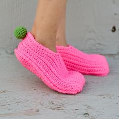 a woman's feet in pink crocheted slippers with green pom - poms