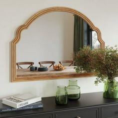 a mirror on the wall above a dresser with vases and flowers in front of it