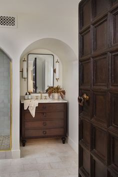 an arched doorway leads to a bathroom with a sink, mirror and shower stall in the corner