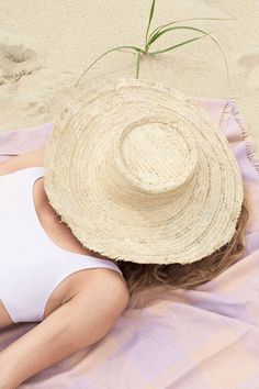 Woven hat on top of model's head that's laying down with a pink and purple fabric on the beach. Summer Beachwear Straw Hat For Travel, Beachy Straw Hat For Travel, Summer Travel Straw Hat Beachwear, Summer Travel Straw Hat In Beachwear Style, Summer Fedora Panama Hat Made Of Palm Leaf, Beachy Sun Straw Hat For Travel, Beachwear Straw Hat For Vacation Travel, Brimmed Straw Hat For Sunbathing On Vacation, Beachwear Straw Hat For Travel And Vacation