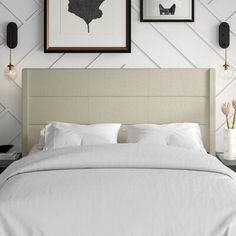 a bed with white sheets and pillows in front of two framed pictures on the wall