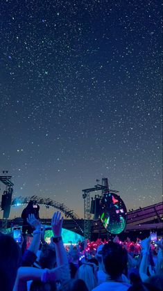 people at an outdoor concert under the night sky with their hands up in the air