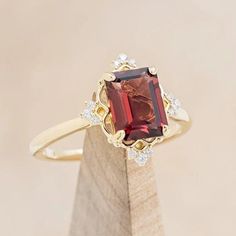 a ring with a large red stone surrounded by small white diamonds on a wooden stand